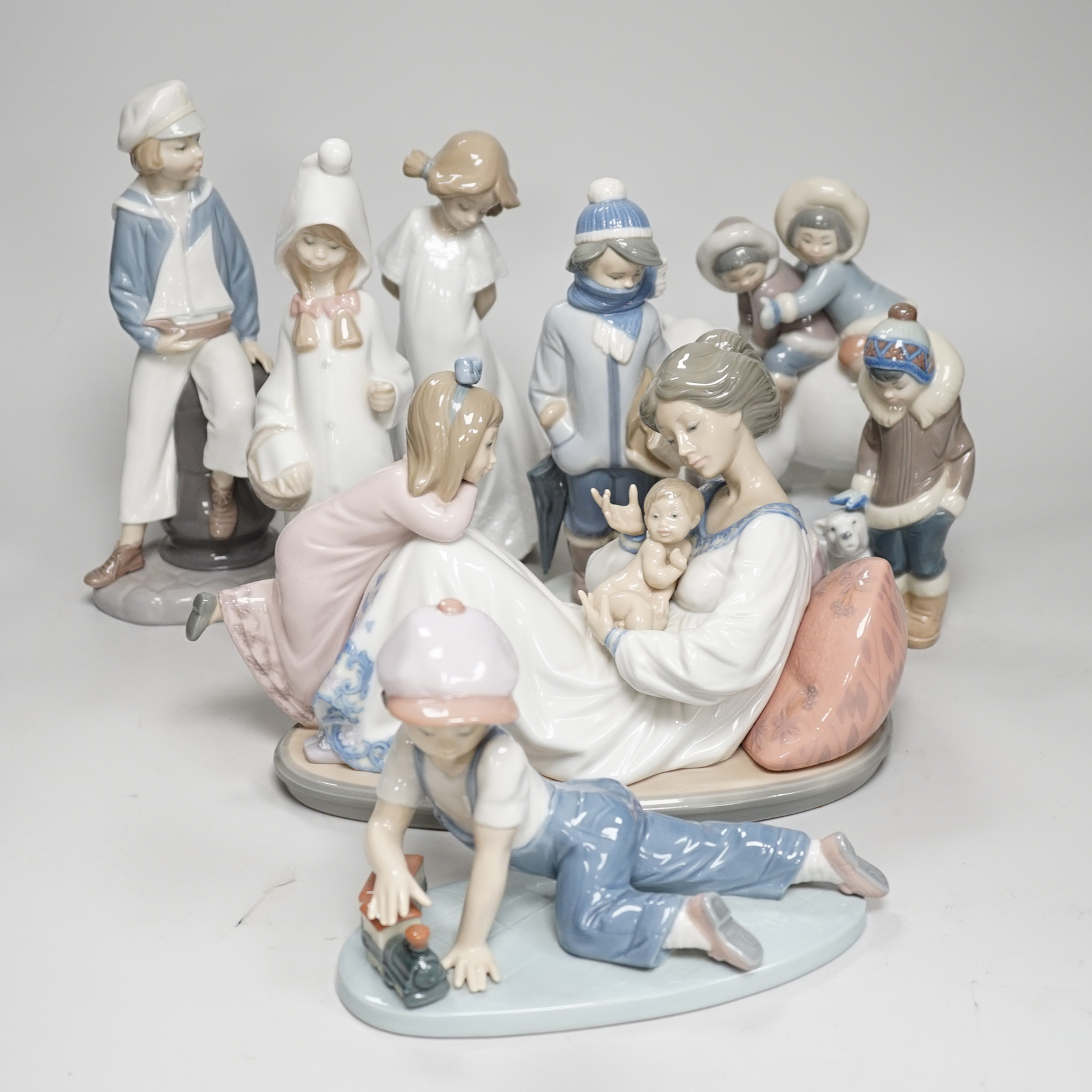 Seven Lladro figures; mother baby and child, boy with train, boy with sailing boat, Eskimo children on a polar bear and four others including a Nao example, the largest 28cm wide